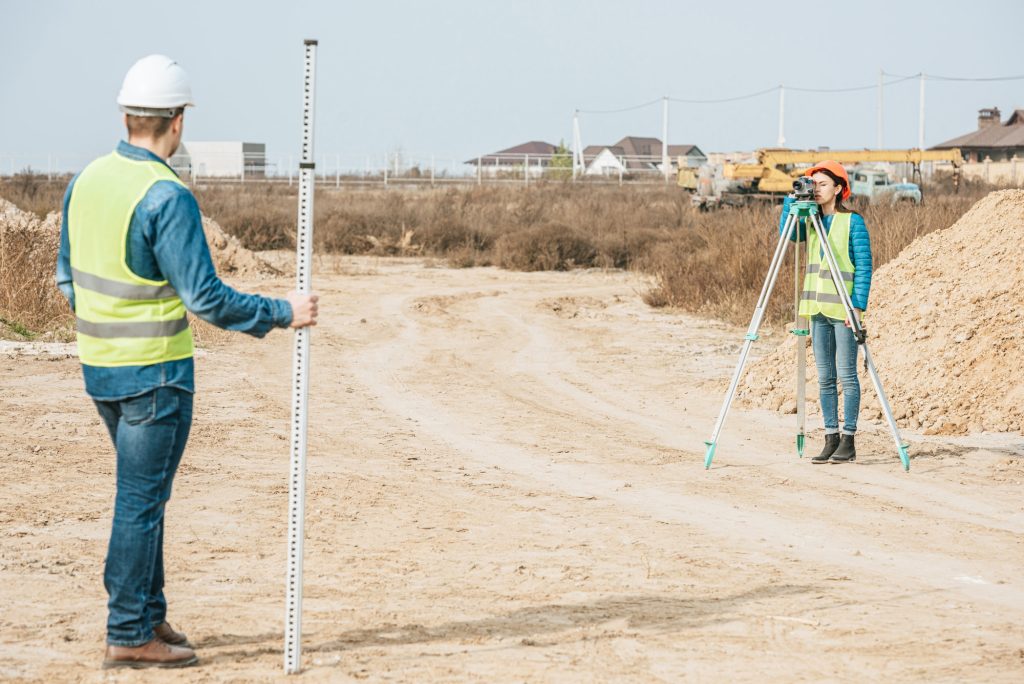 Surveyors with digital level and survey ruler working on dirt road